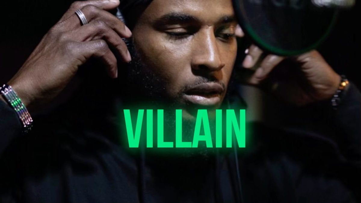 Silent 777 in black, looking down with his hands on his headphones, with the word VILLAIN glowing green across the front.