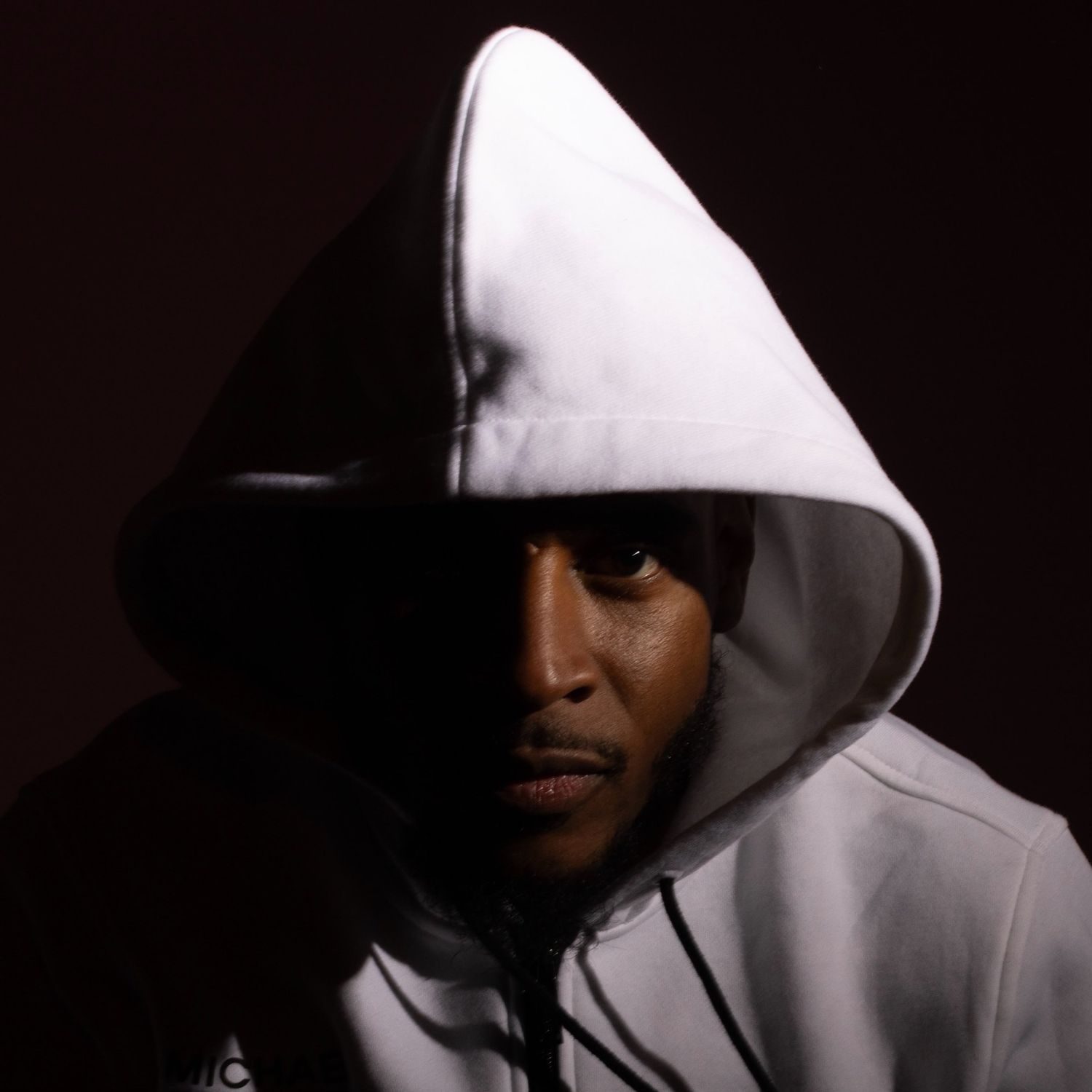 Silent 777 in a white hoodie with the hood up, half of his face in shadow against a dark background.