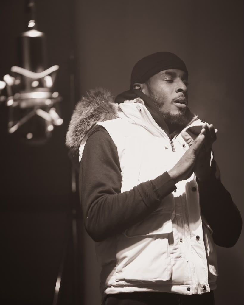 Silent 777 in a white vest with a fur hood, performing in front of a studio microphone.