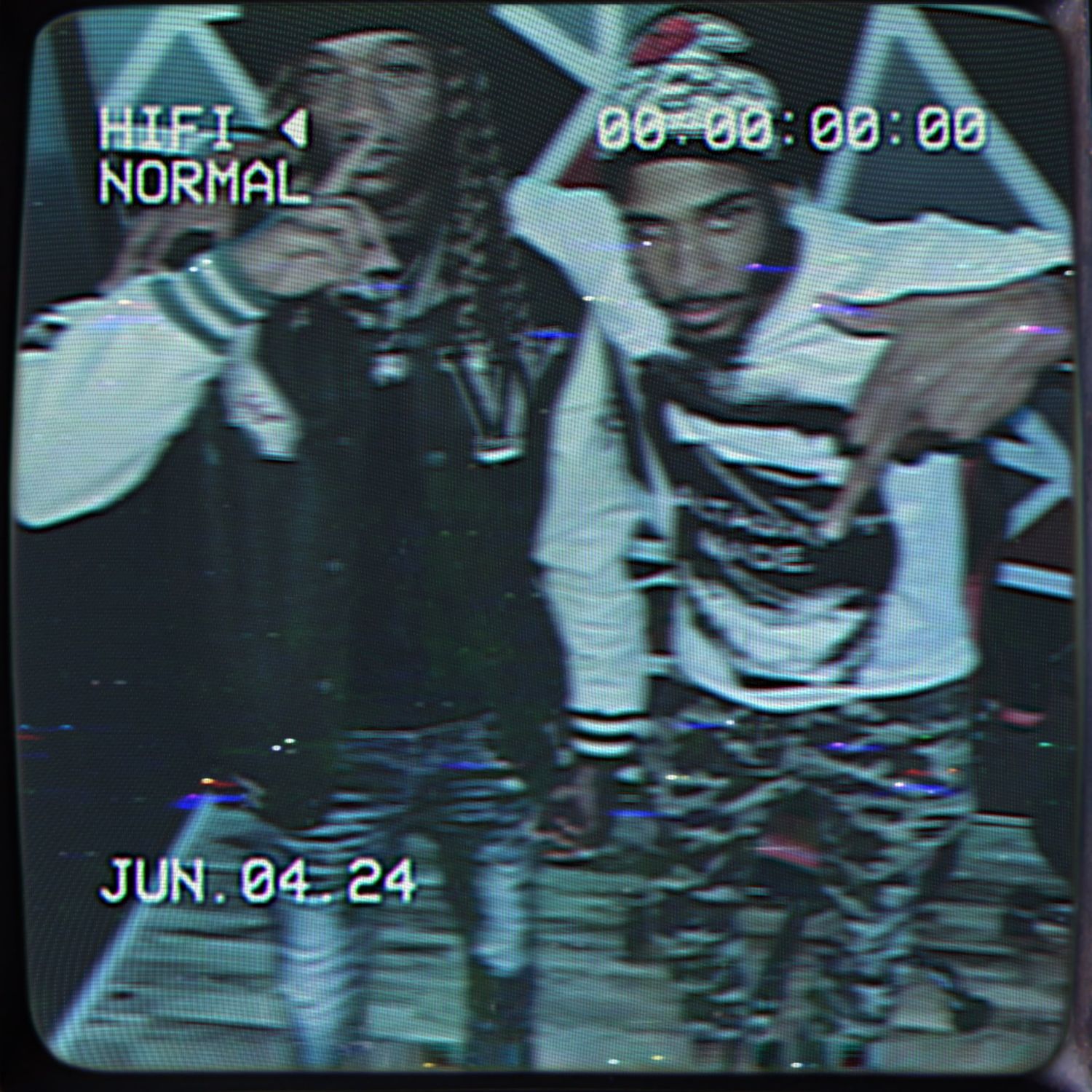 A grainy camcorder still of Silent 777 and a friend, both with a hand raised, with a date stamp reading June 04 24.