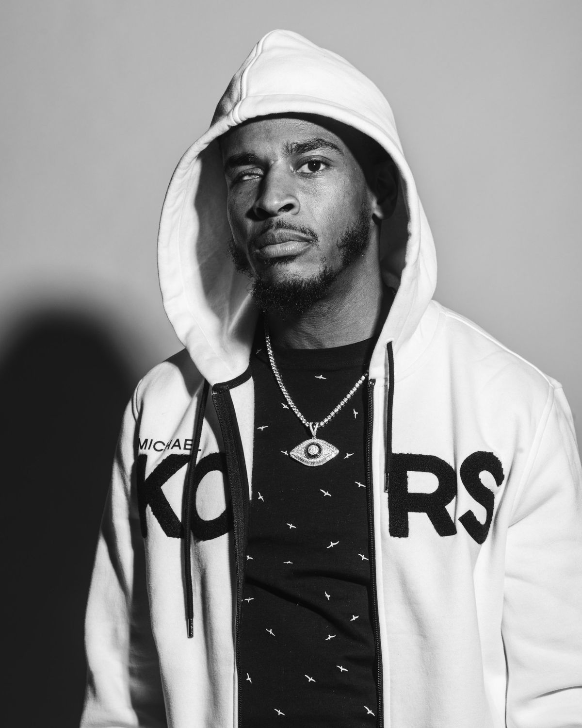 Black and white portrait of Silent 777 in a white hoodie with the hood up, wearing an eye pendant.